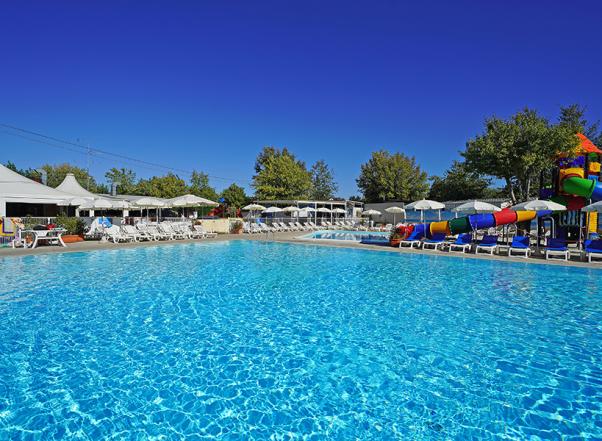 Piscina all'aperto con scivoli colorati e lettini sotto ombrelloni.